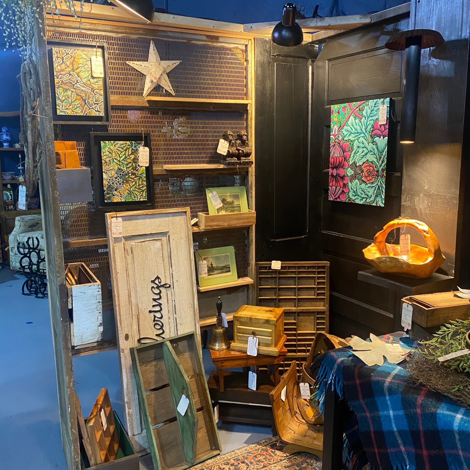 Shelves of layered objects at the Futurology booth — framed art, salvaged doors, wool, pottery and warm lamp light