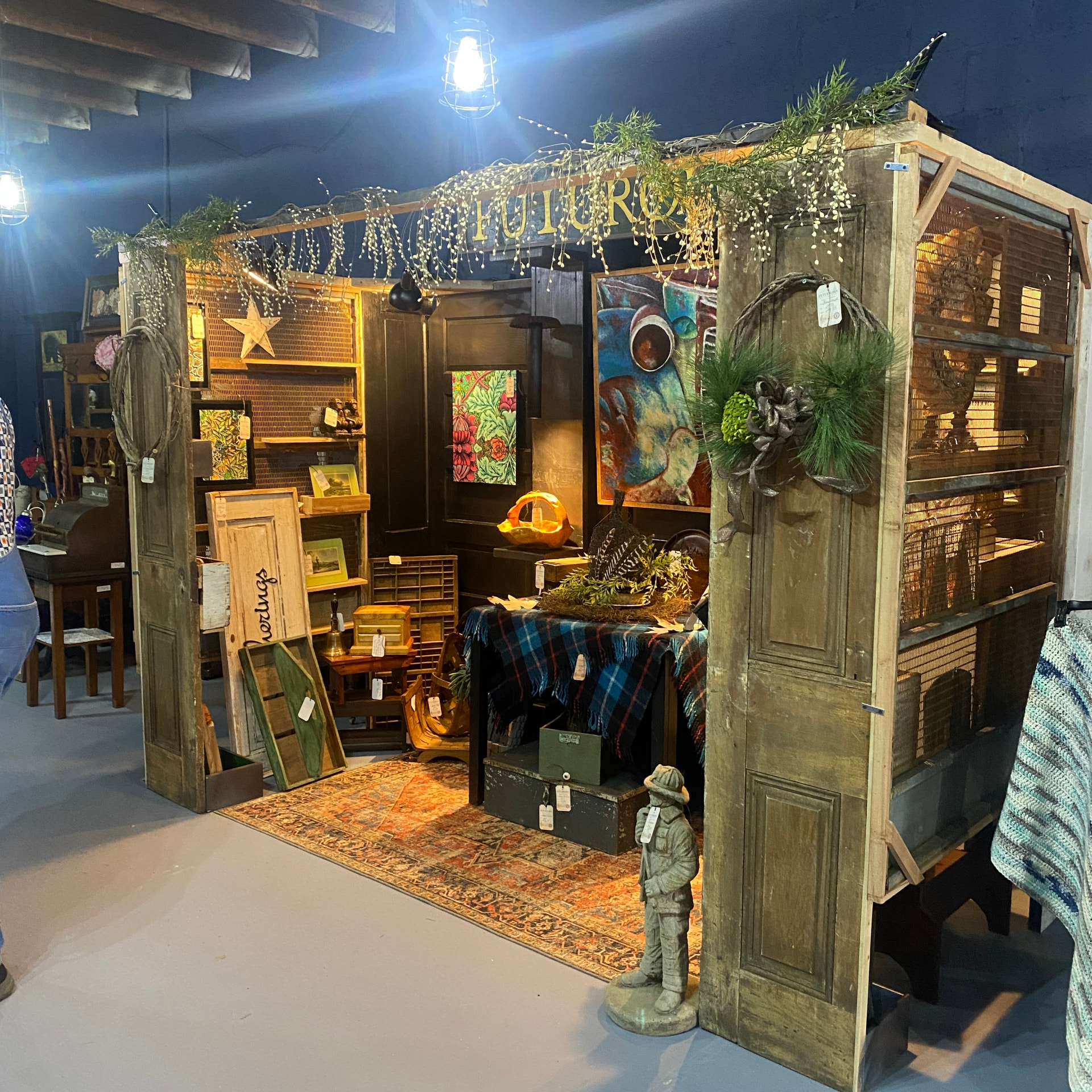 The full Futurology booth seen from the aisle — salvaged doors, rugs, framed art and lamplight
